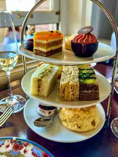 Image of the iconic tea service at the Empress Hotel in Victoria, Canada. Three tiered tea tray with scones and jam on the lower tier, tea sandwiches on the middle tier, and decadent sweets on the top tier.