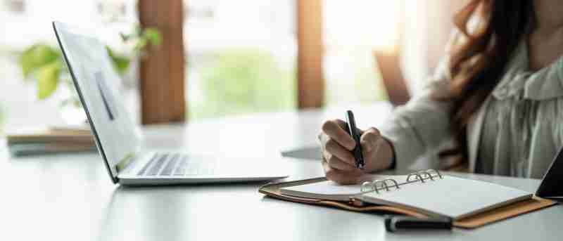 Image of a woman working on both a computer and writing in a notebook