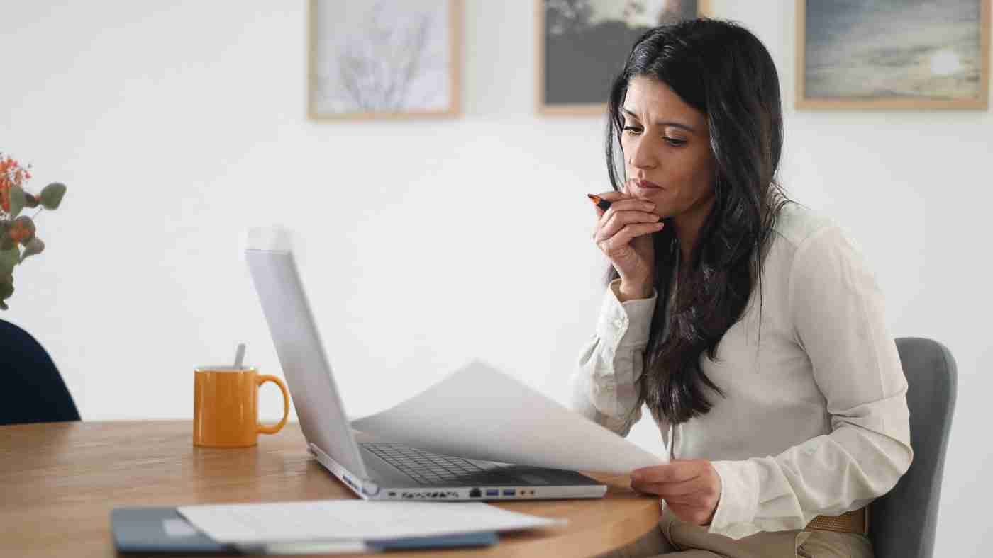 Woman working on a computer and referring to written pages.