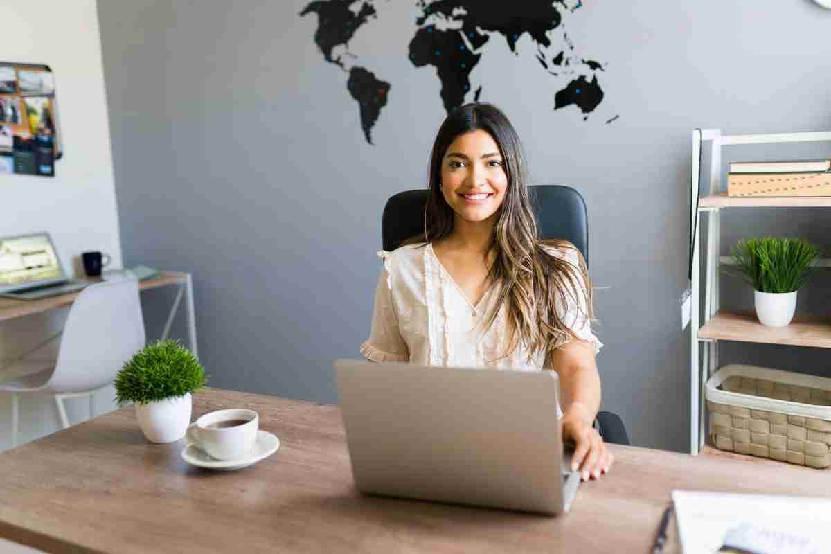 Portrait of a cheerful travel agent sales representative sitting behind her desk with world map on the background