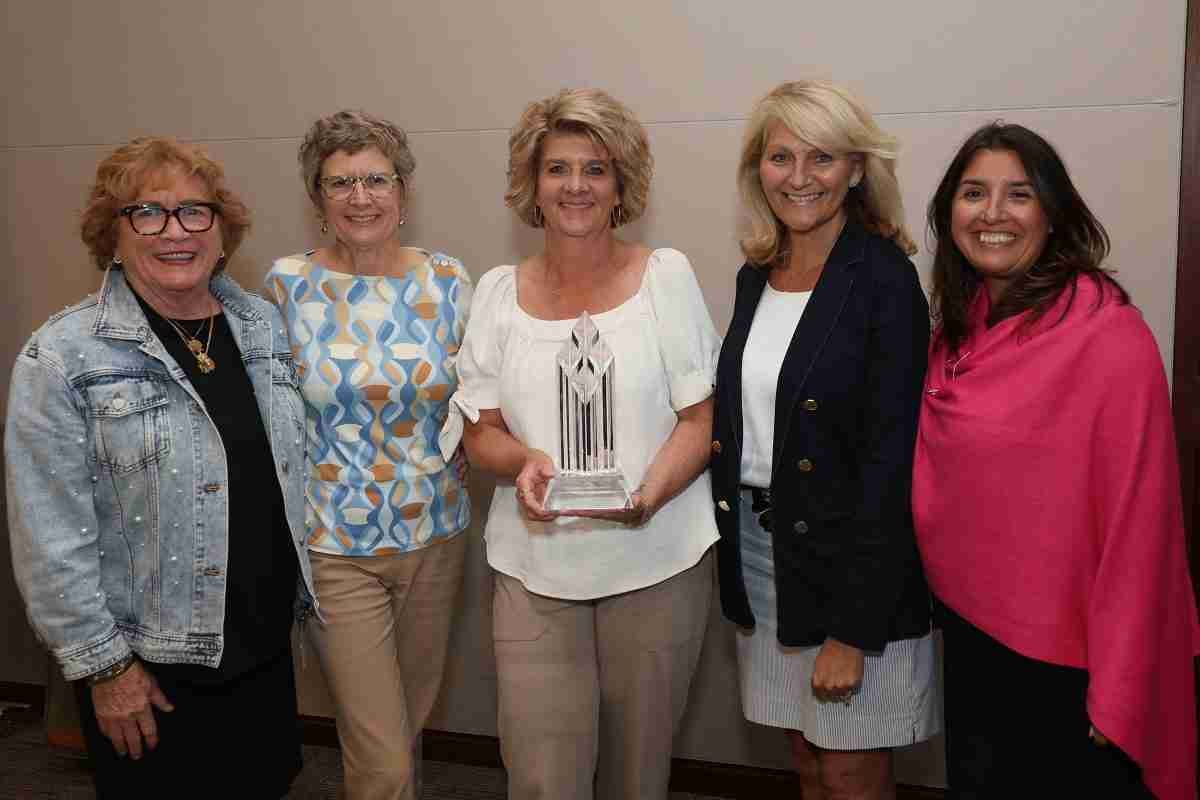 Five women stand side by side, smiling, as the center woman holds The Travel Institute’s 2025 Education Excellence Award.