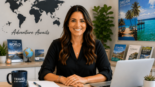 Brunette woman sits behind desk with laptop open. Besider her is a notebook and coffee mug that reads, "Travel is my Therapy". Along the walls are books on travel destinations. There is a poster of a tropical area on one wall and the other has a world map with the words, "Adventure Awaits" behind her.